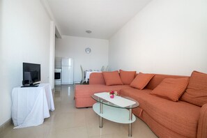A living room with a sofa, a glass coffee table, a TV on a side table, and a refrigerator in the background. - Apartments Galic (Omis)