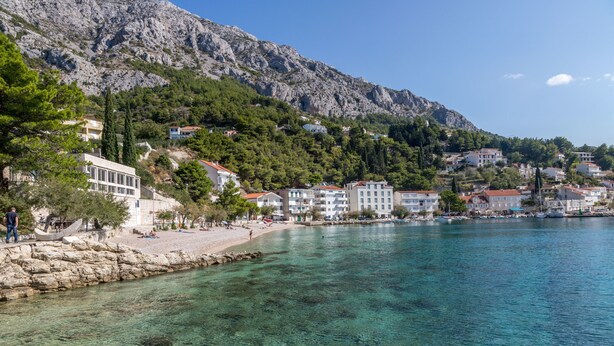 A coastal town with clear waters, buildings along the shore, and a mountainous backdrop. - Apartments Gordana (Mimice)