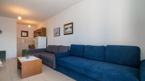 A living room with a blue sofa, a wooden coffee table, a grey sofa, and a small plant. There are two framed pictures on the wall. - Apartments Gordana (Mimice)