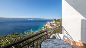 A balcony with a table and chairs, overlooking a coastal town and the sea. - Apartments Gordana (Mimice)