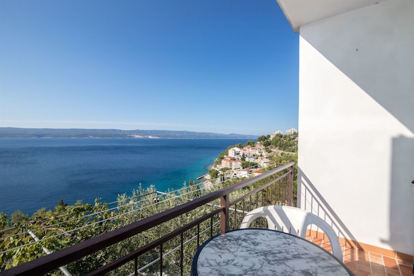 Un balcone con tavolo e sedie, vista su una cittadina costiera e il mare.