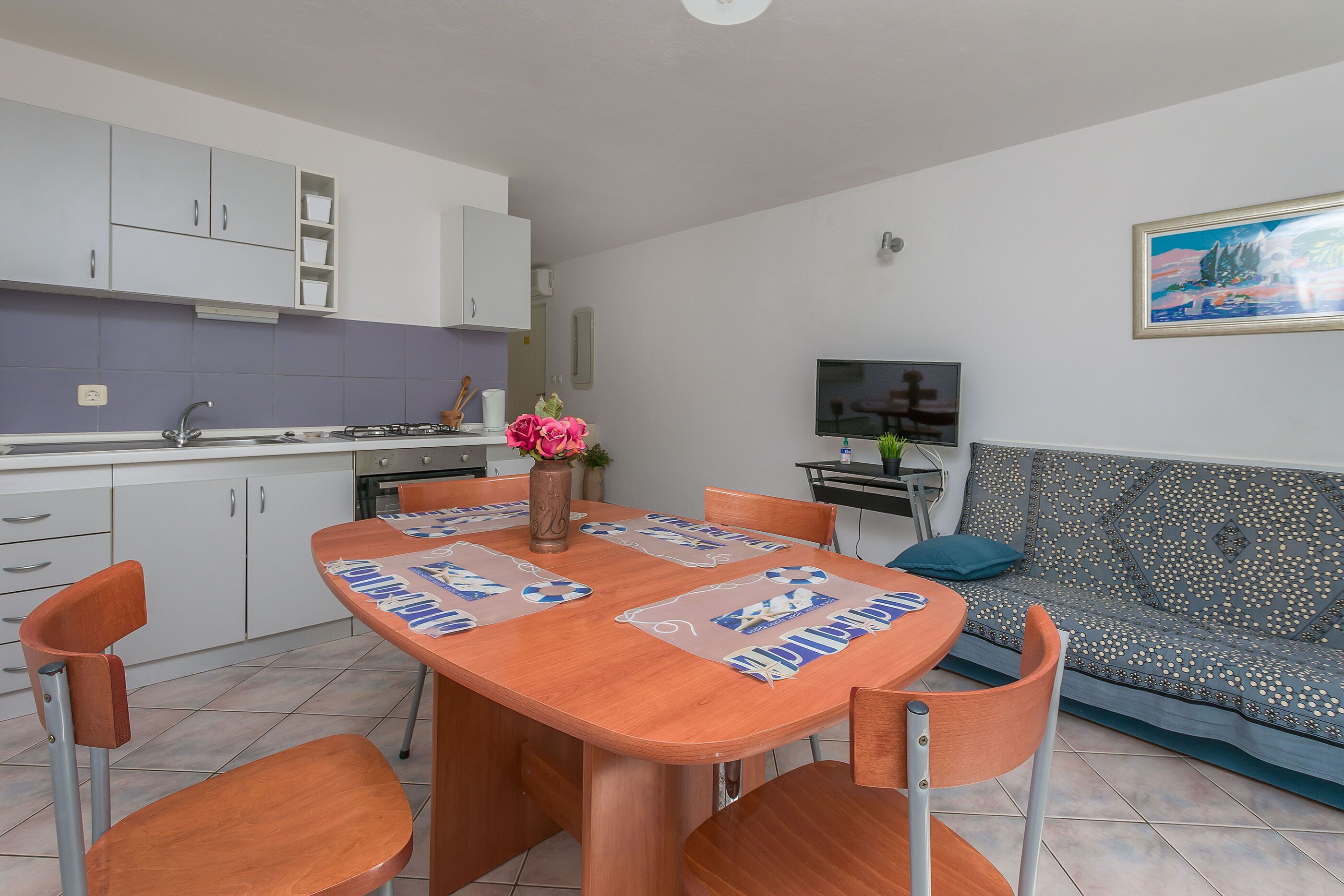 A modern kitchen with white cabinets, a dining table with placemats, and a sofa with a patterned cushion.