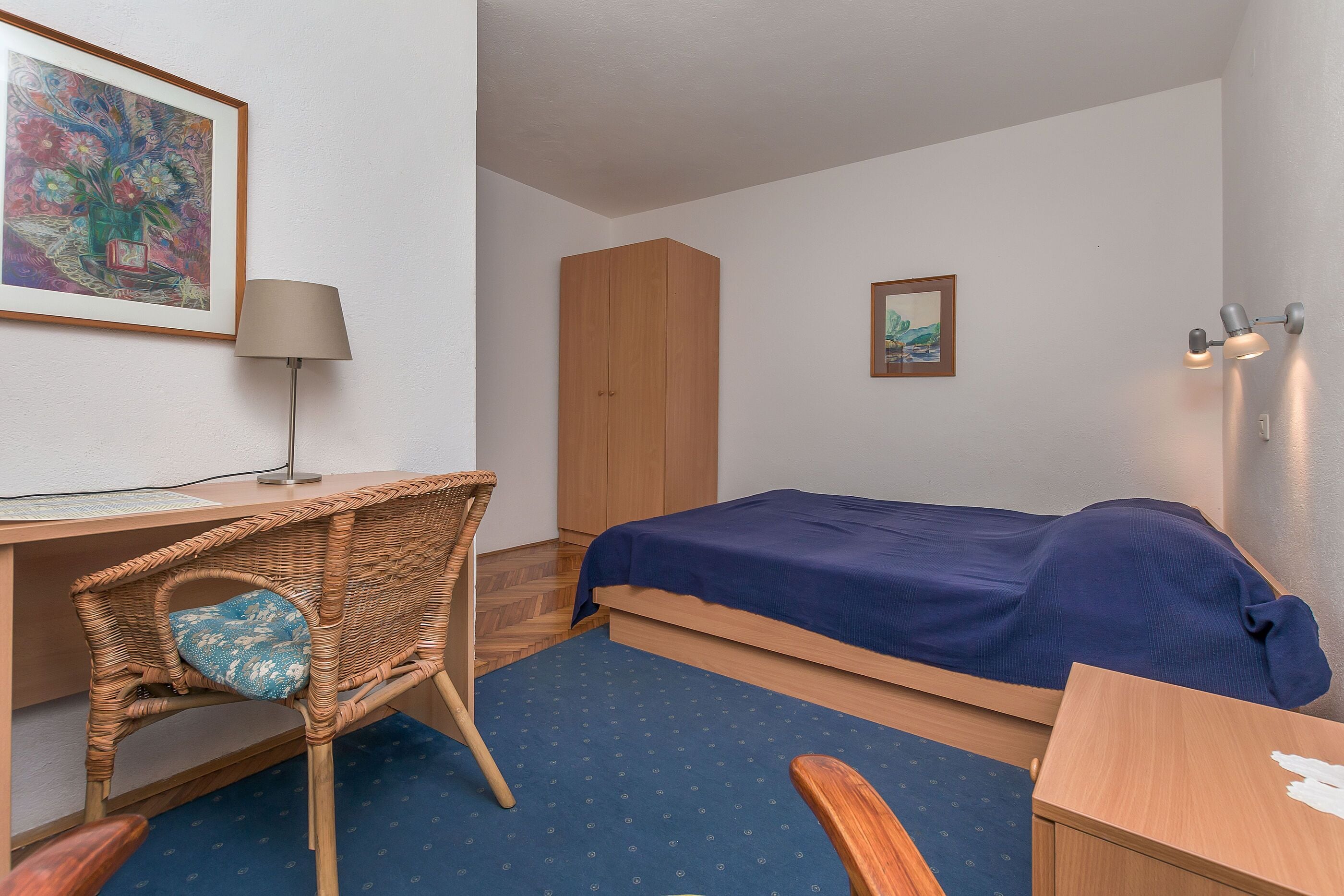 A bedroom with a bed, a desk, a chair, a wardrobe, and a lamp.