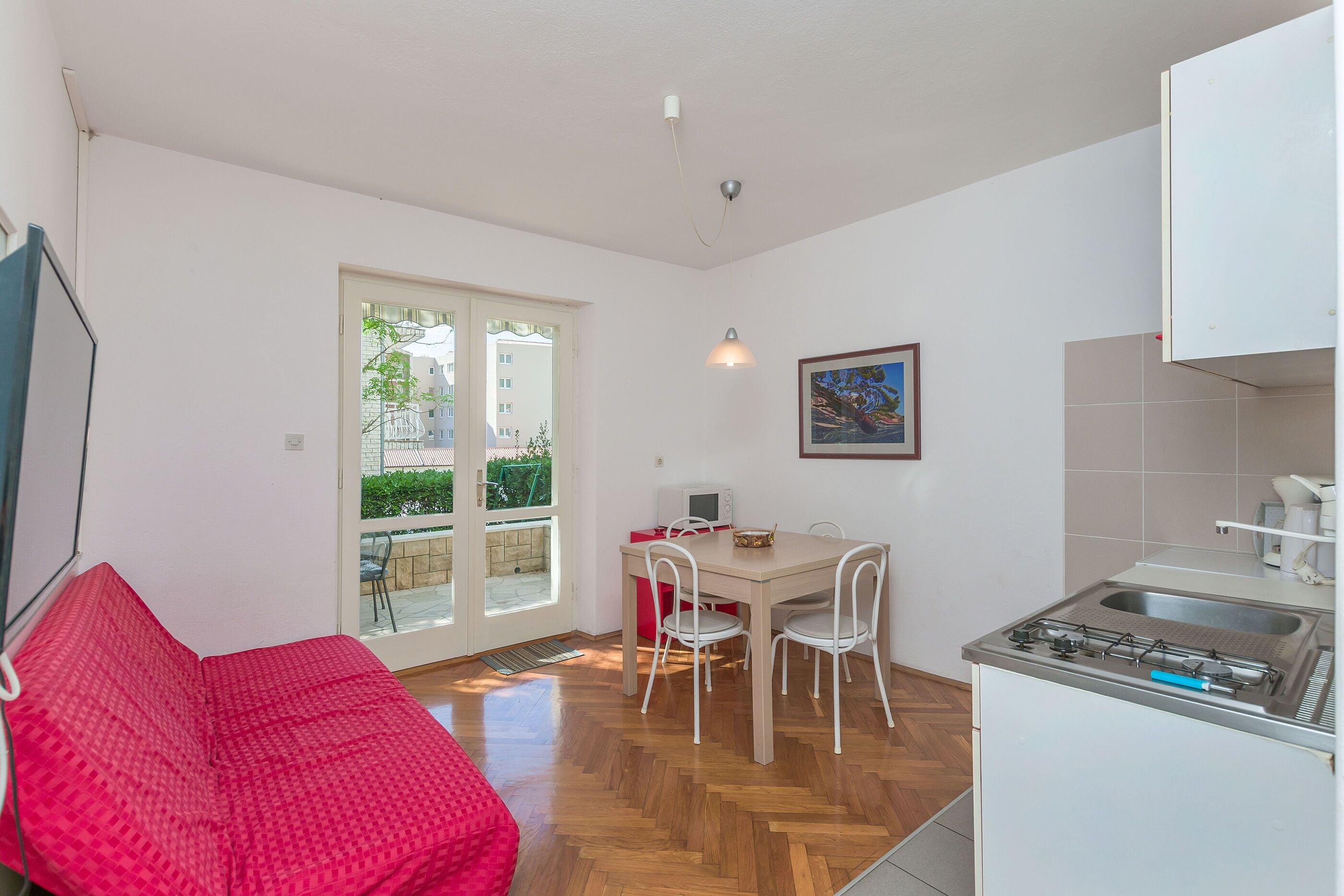 A compact kitchen with a dining area, a red sofa, and a view through the glass door.