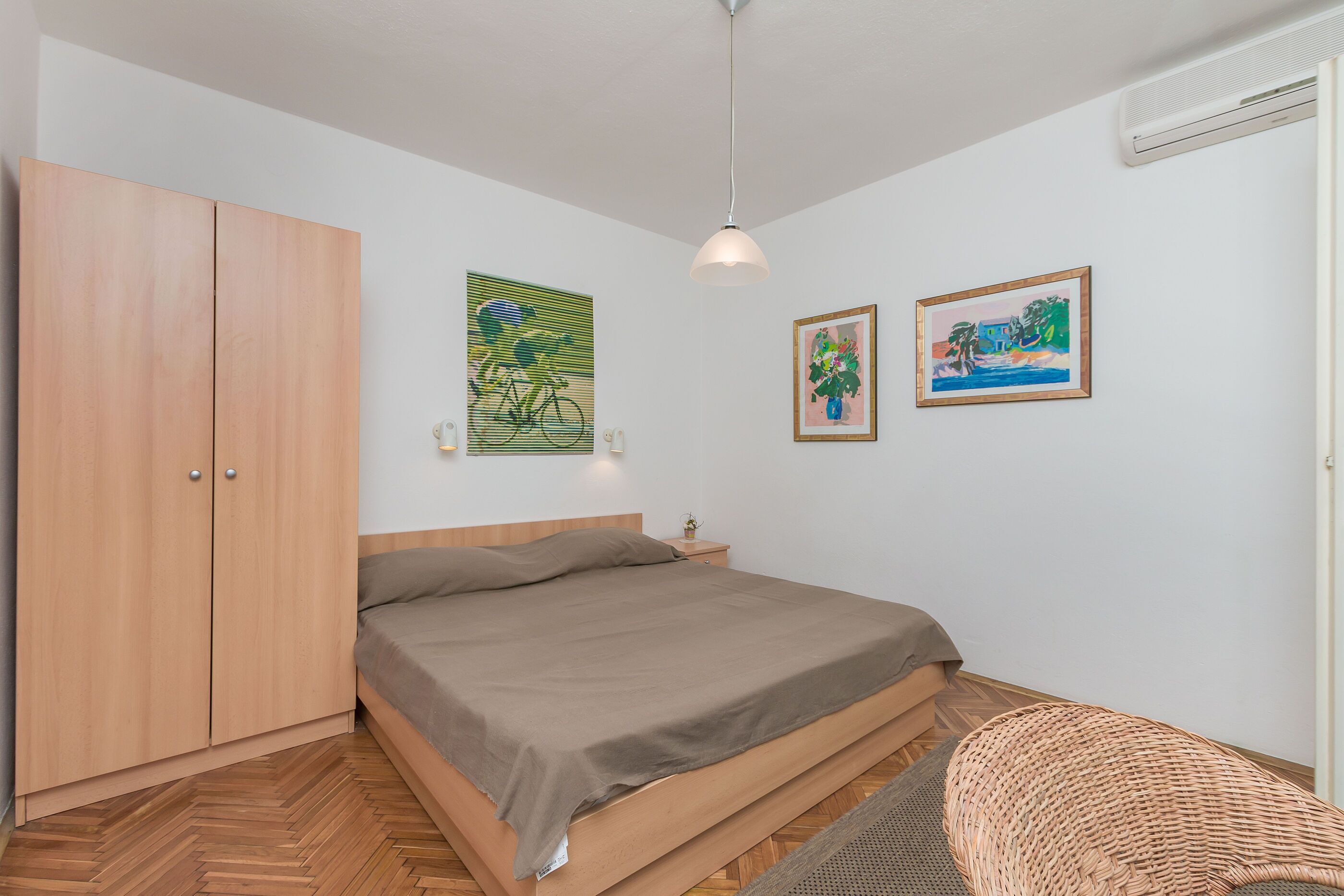 A bedroom with a bed, wooden wardrobe, and two wall-mounted pictures.