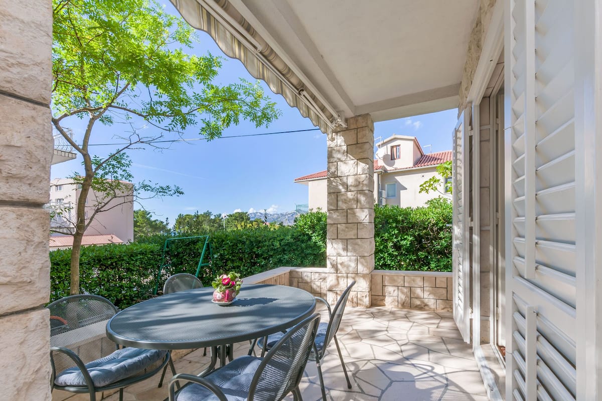 An outdoor patio with a round table and chairs, stone pillars, and a view of a building in the background.
