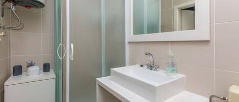 A bathroom with a white sink, a mirror, and a shower enclosure.