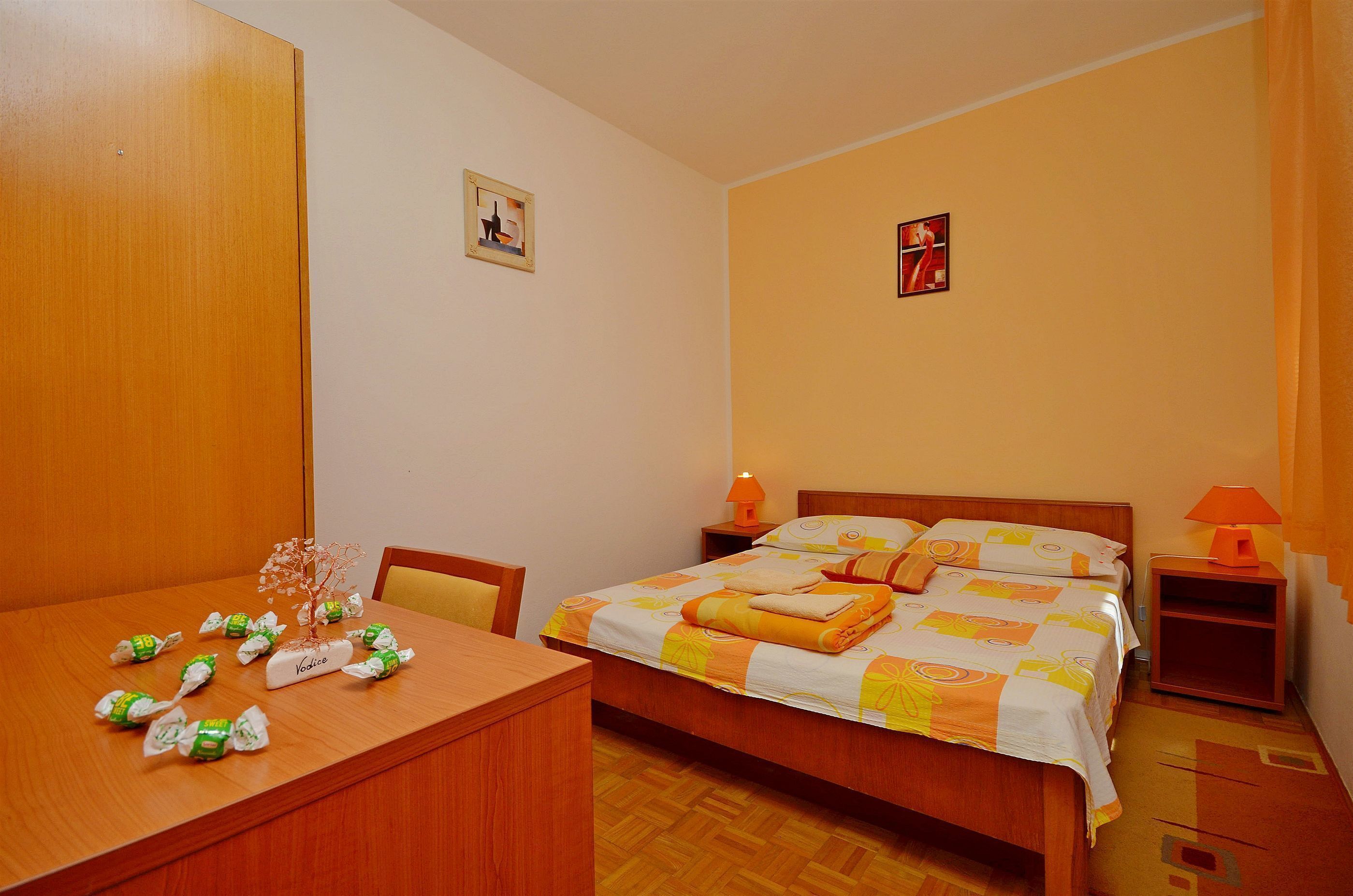 A hotel room with a wooden bed, a desk with a chair, and a small table with wrapped gifts.
