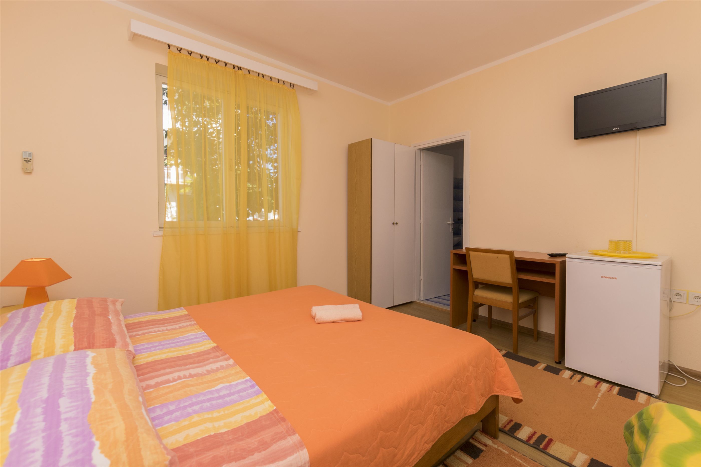 Una habitación de hotel con cama, escritorio, silla, televisor y refrigerador.