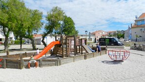 Ein Spielplatz mit Rutsche und Klettergerüsten, umgeben von Bäumen und Gebäuden.