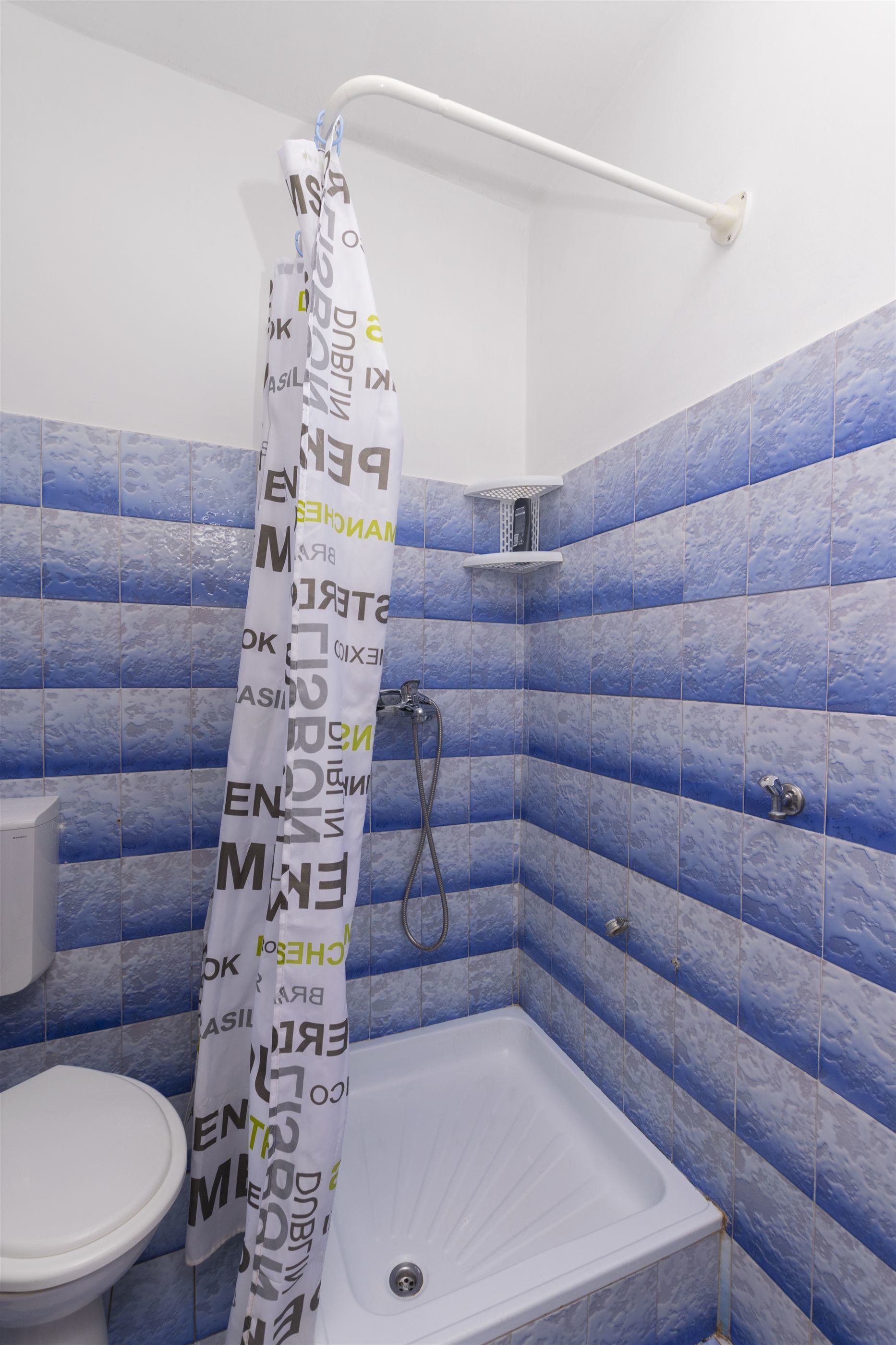 A bathroom with a shower curtain, a bathtub, and blue-tiled walls.