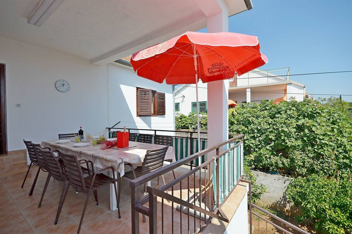 An outdoor dining area with a table, chairs, and a red umbrella.