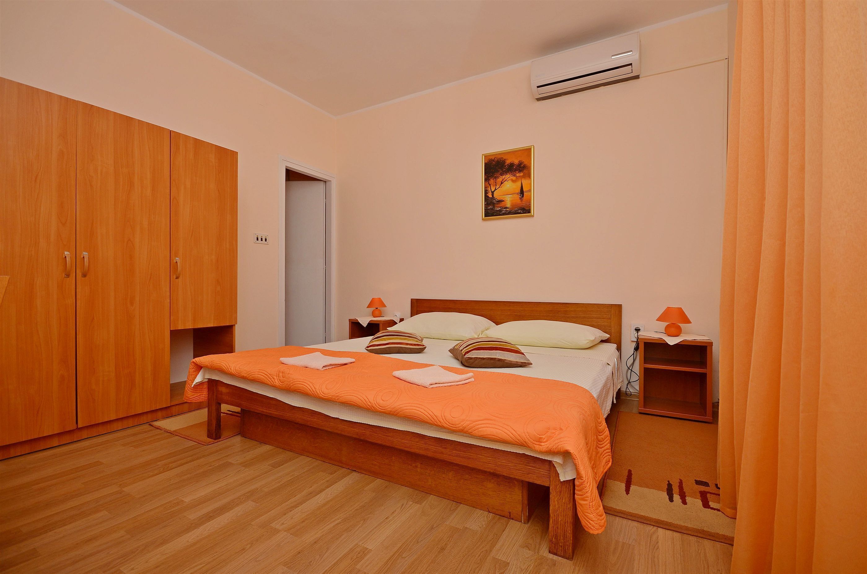 Ein Schlafzimmer mit einem hölzernen Bett, einer Klimaanlage, einem Nachttisch mit Lampe und einem Kleiderschrank.
