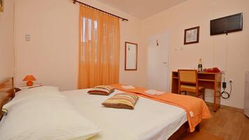 Una camera d'albergo con due letti, una tenda arancione, una scrivania con una sedia, una televisione e un quadro appeso al muro.