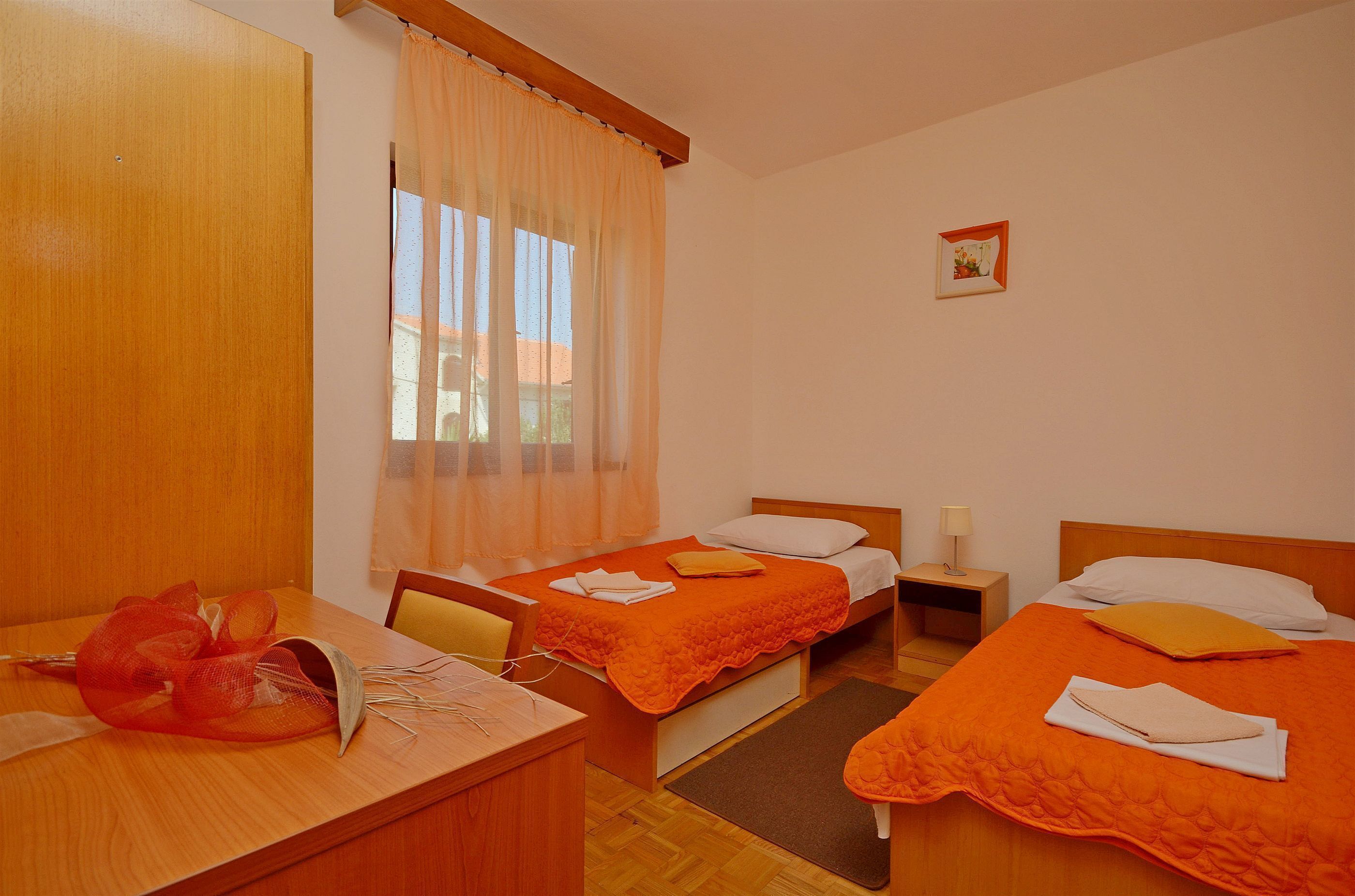 A hotel room with two beds, a wooden desk, and a window with sheer curtains.