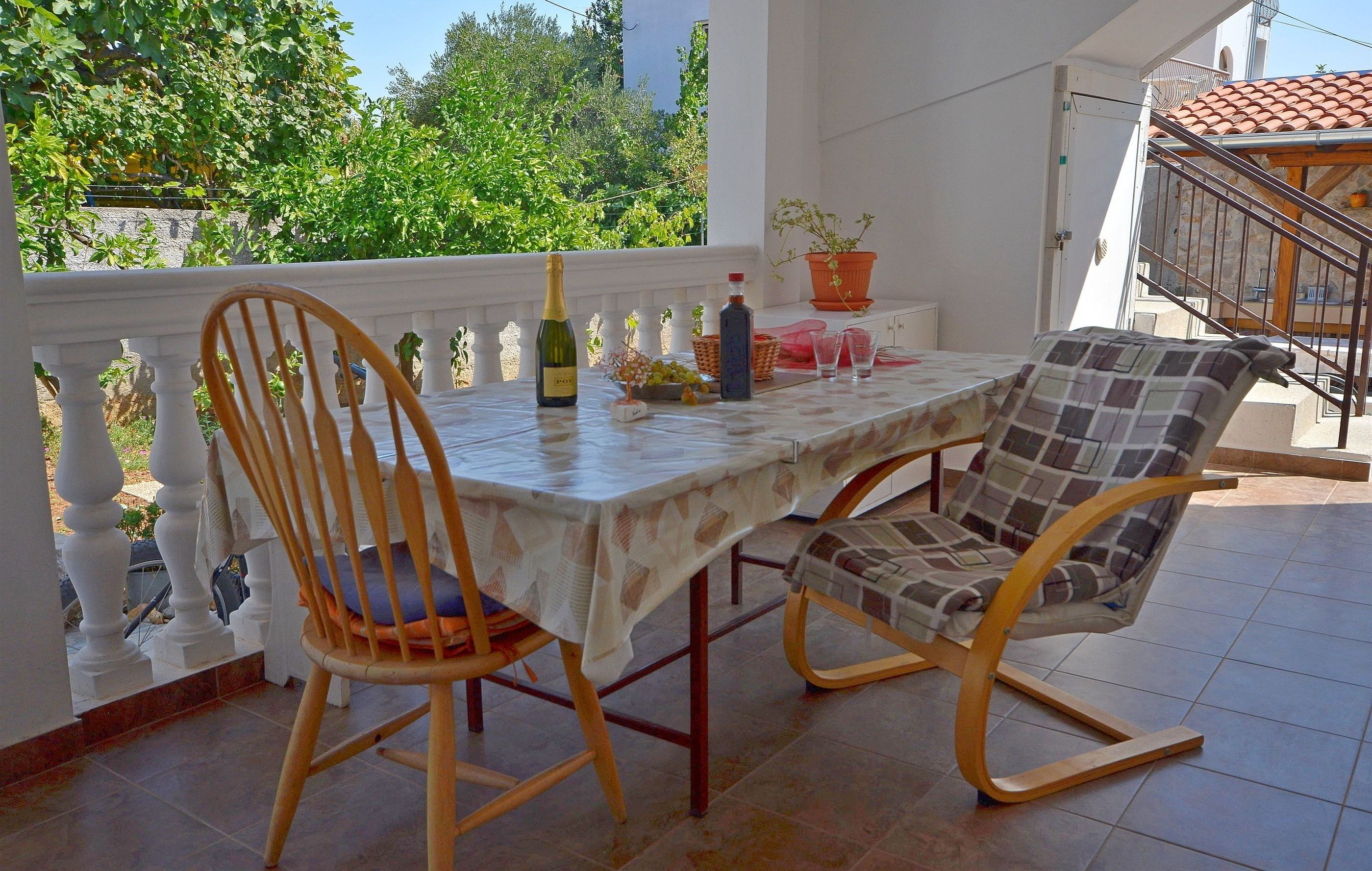 Una terraza con una mesa, dos sillas, una botella y una cesta de fruta.