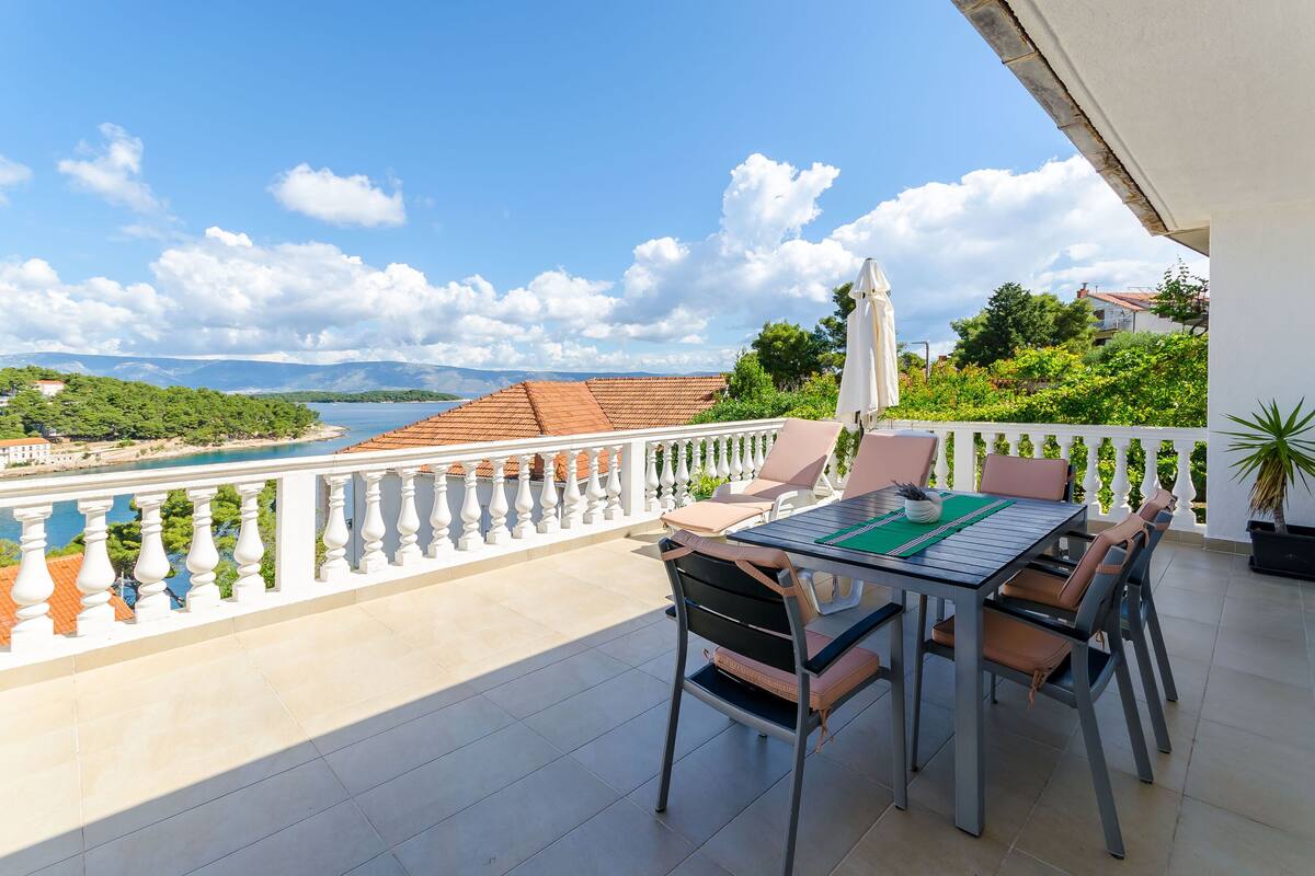 A balcony with a table and chairs, overlooking a body of water and greenery.