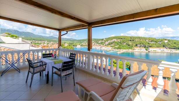 A balcony with a table and chairs, overlooking a coastal town and a body of water. - Apartments Jakov (Jelsa)