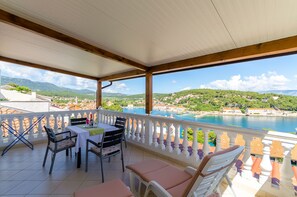Un balcó amb taula i cadires, vista a una vila costanera i una extensió d'aigua.