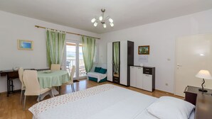 A hotel room with a bed, a desk with a chair, a wardrobe, and a small table with a lamp. - Apartments Jakov (Jelsa)