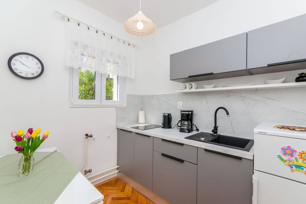 A modern kitchen with grey cabinets, a white countertop, a black sink, a coffee maker, and a refrigerator with a colorful sticker.