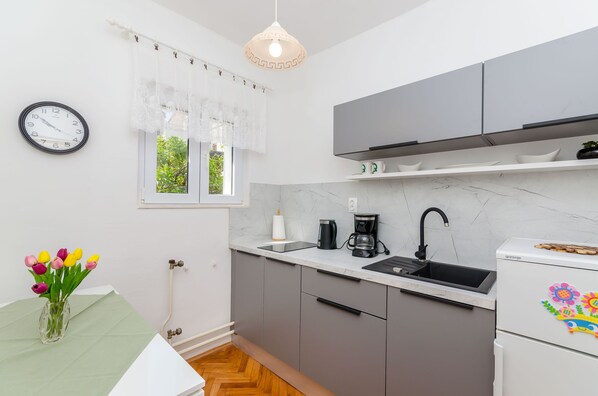 Eine moderne Küche mit grauen Schränken, einer weißen Arbeitsplatte, einer schwarzen Kaffeemaschine und einem weißen Kühlschrank mit bunten Magneten.
