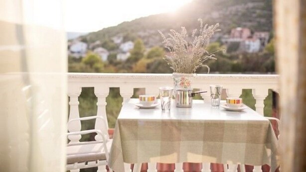 A balcony with a table set for dining, a chair, and a view of a mountain and houses in the background. - Apartments Mirko (Seget Vranjica)