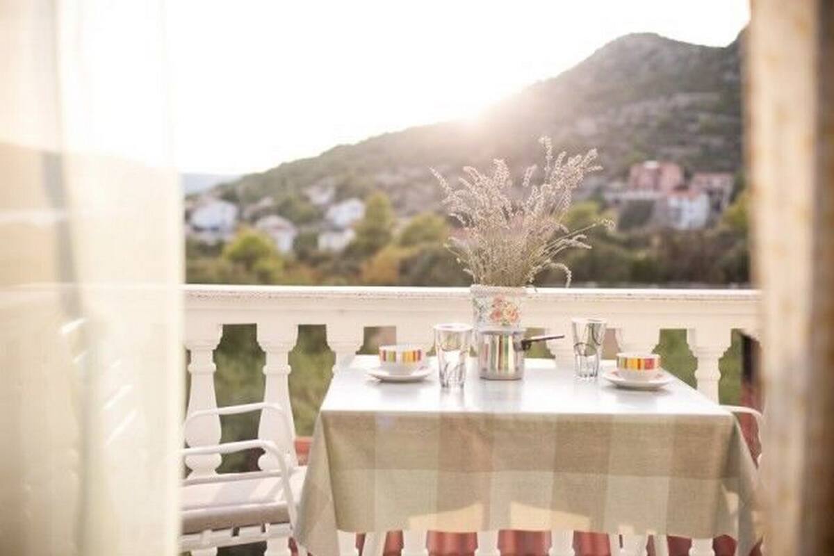 Ein Balkon mit Esstisch, Stuhl und Blick auf Berge und Häuser im Hintergrund.