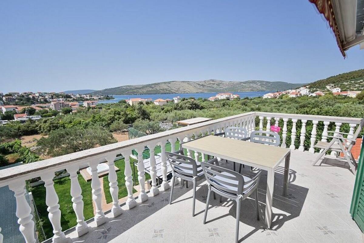Ein Balkon mit Tisch und Stühlen mit Blick auf eine Küstenstadt und das Meer.