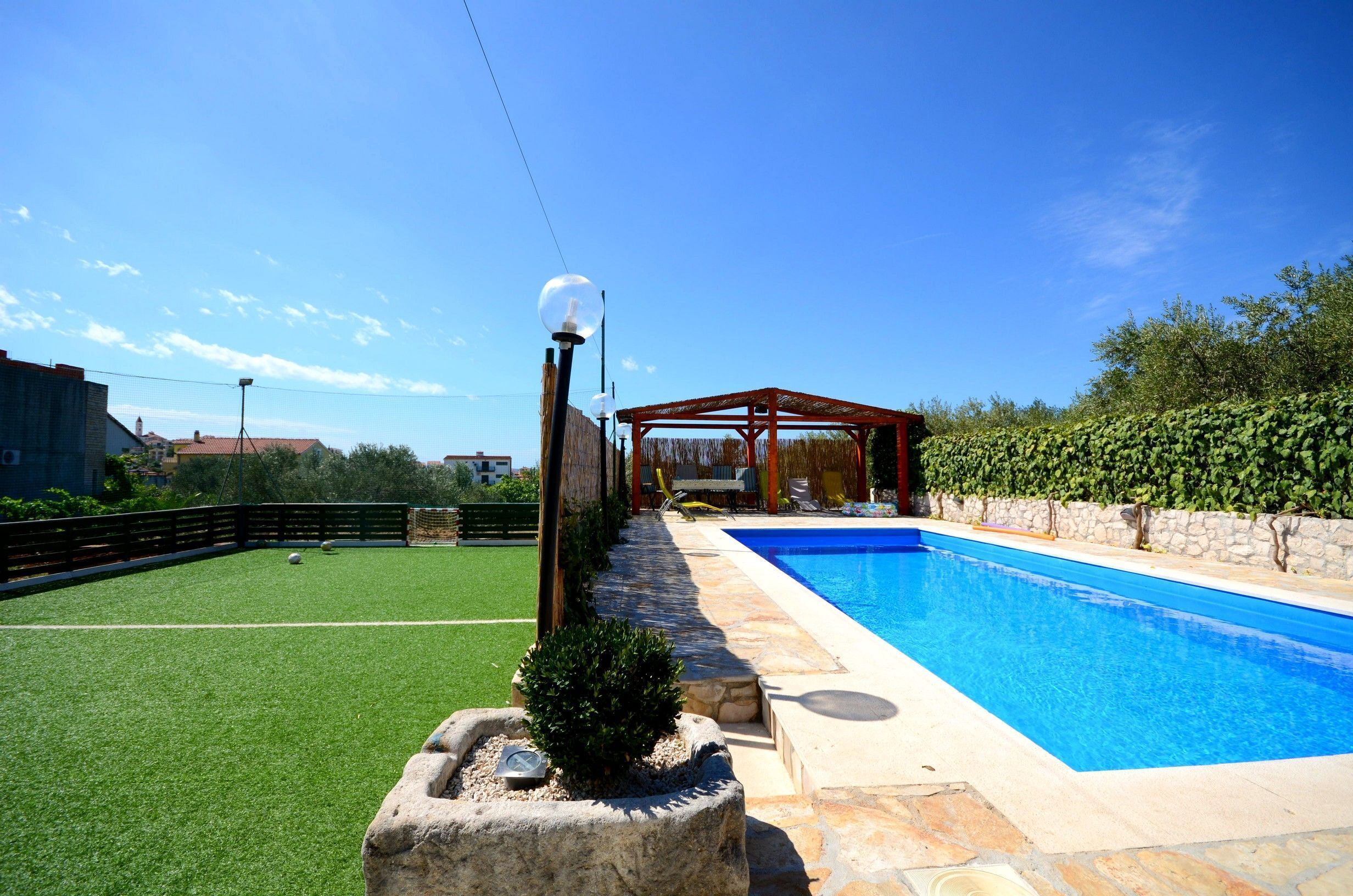 Ein Schwimmbecken mit einer Pergola und einem Rasen.