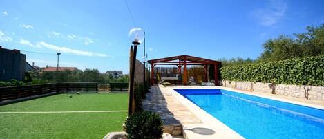Ein Schwimmbecken mit einer Pergola und einem Rasen.