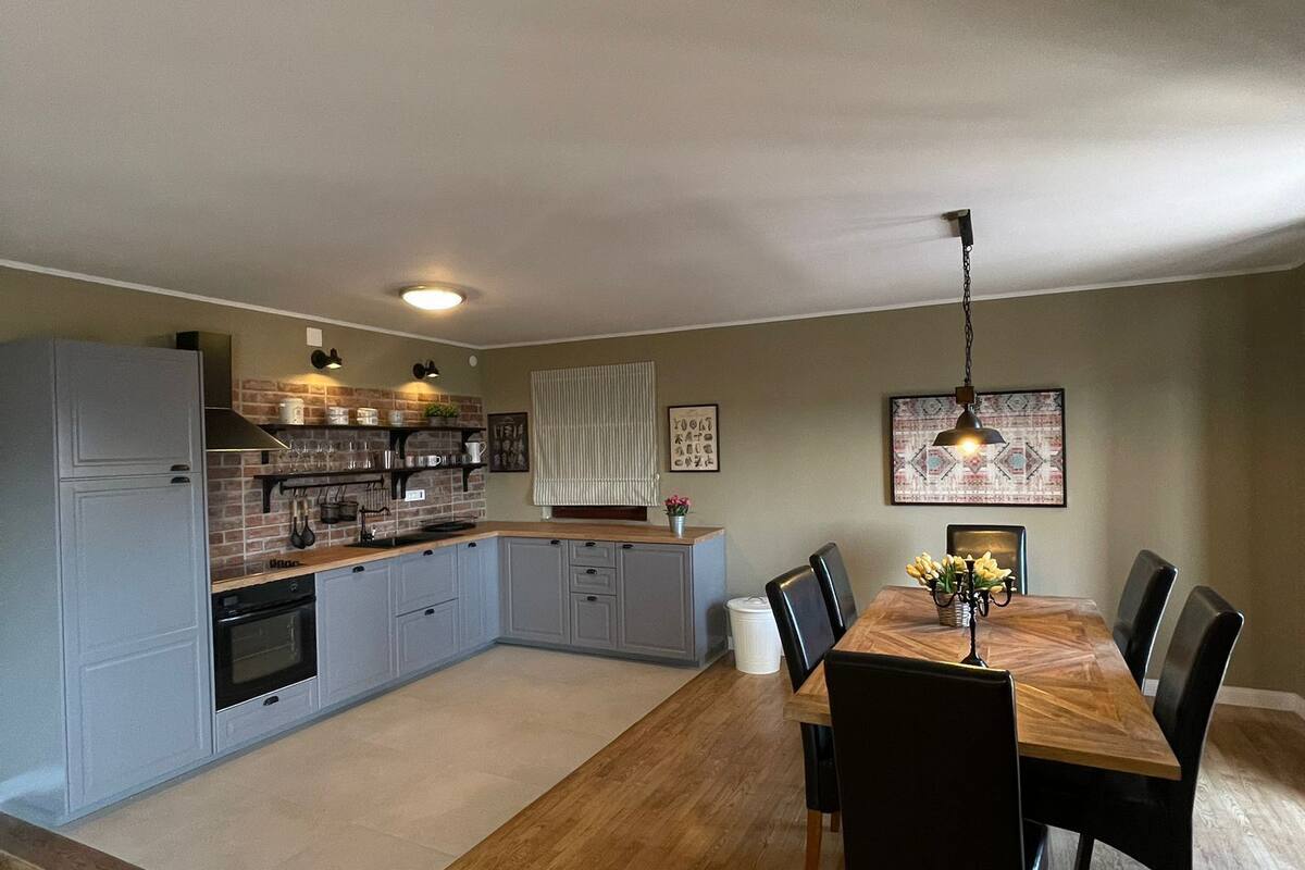 Eine geräumige Küche mit modernen Geräten, ein Essbereich mit Holztisch und -stühlen sowie eine Wand mit Ziegeloptik.