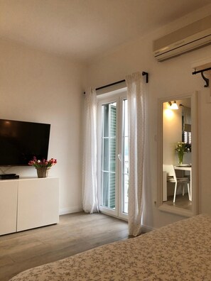 A bedroom with a TV, a bed, a window with curtains, and a view of the outside. - Apartments Mirko (Seget)