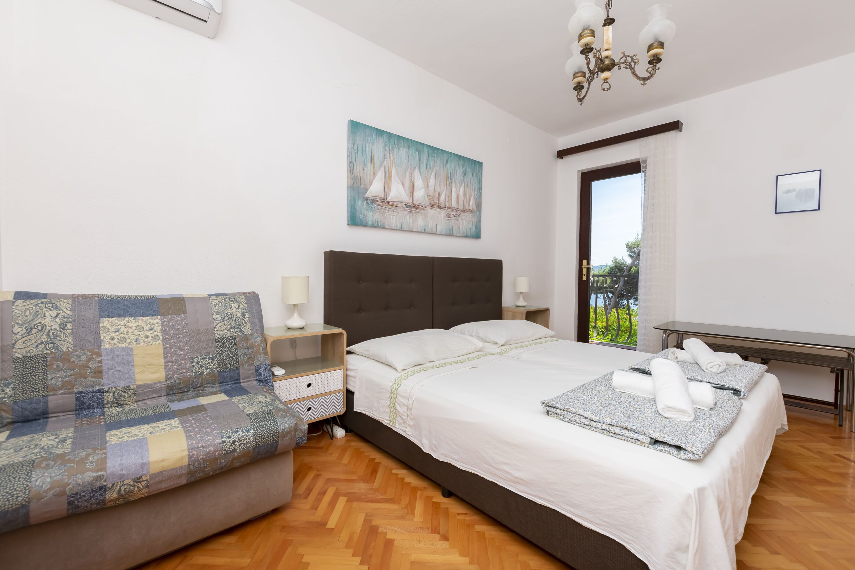 Una camera da letto con un letto, un divano, un comodino, un quadro e vista sul verde.