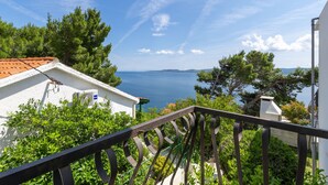 Un balcone con vista sul mare, circondato dal verde e da edifici bianchi.