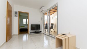 Un soggiorno moderno con TV a schermo piatto, una porta scorrevole in vetro che dà su un'area esterna e un tavolino di legno.