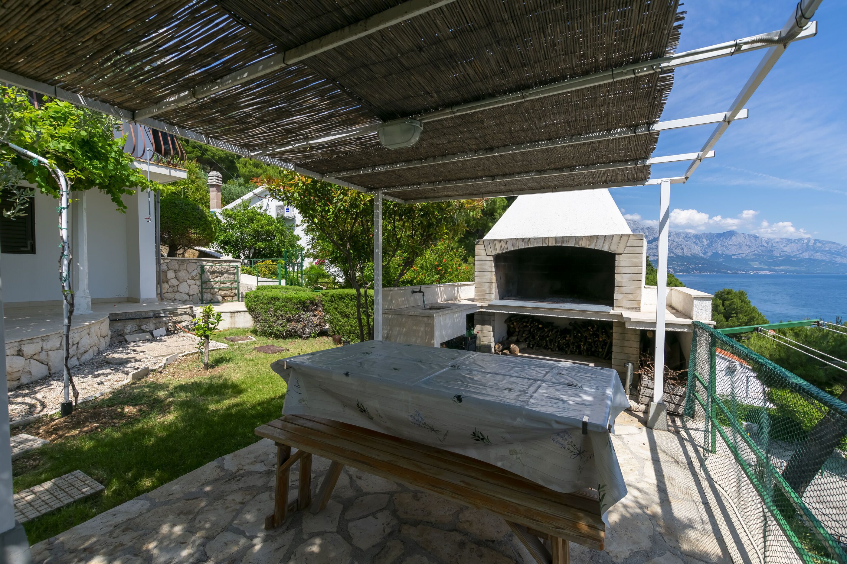 A stone patio with a grill, a pergola, and a view of the sea.