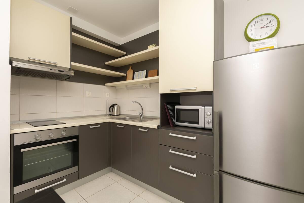 A modern kitchen with a stainless steel refrigerator, built-in oven, microwave, and a kettle on the countertop.