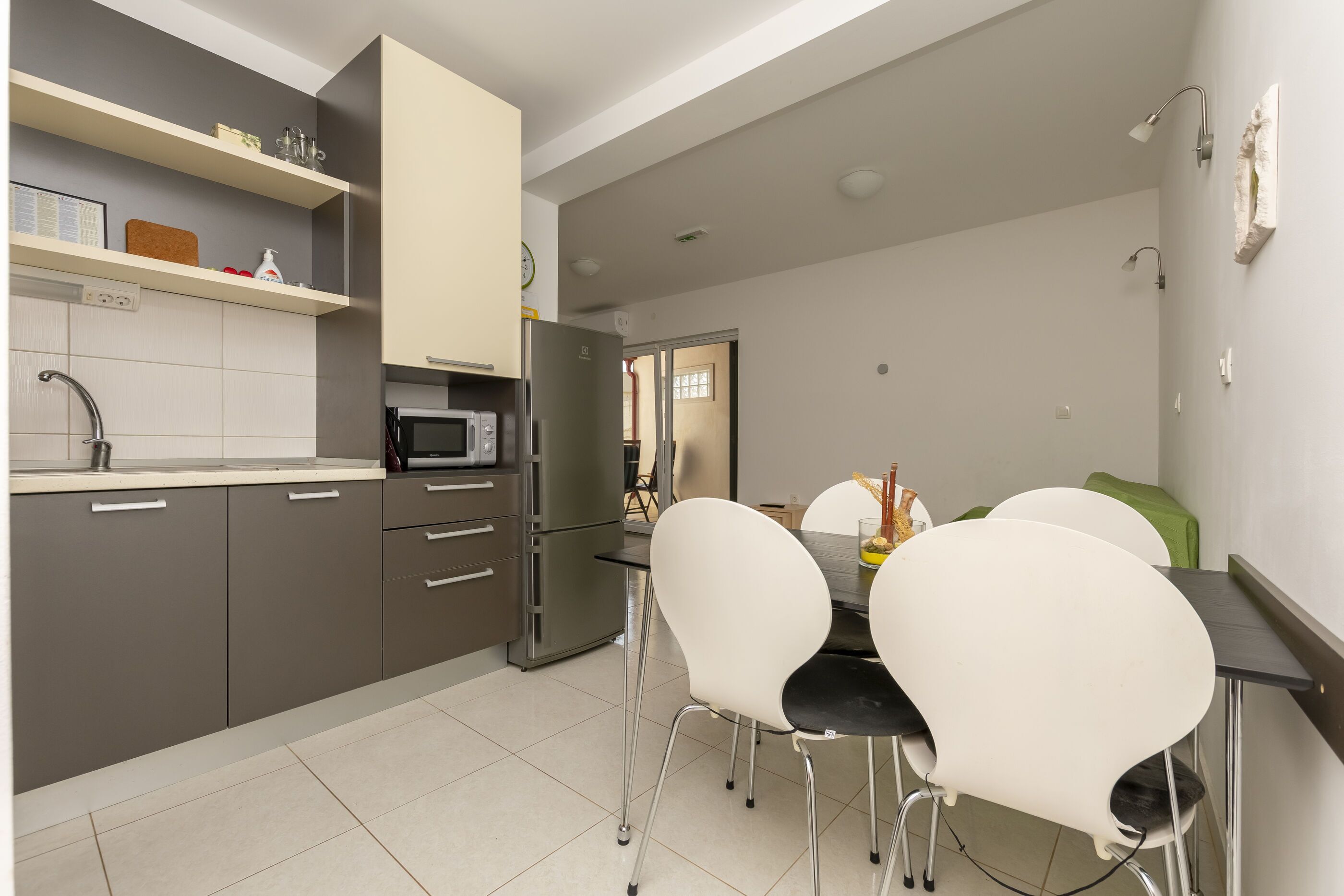 A modern kitchen with grey cabinets, a microwave, and a dining area with white chairs.