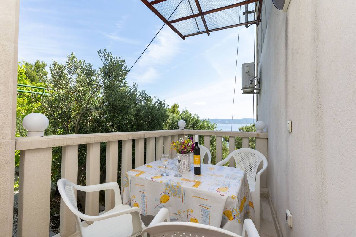 A balcony with a table set for two, a bottle of wine, and a vase with flowers.