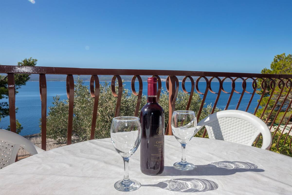 A table with a wine bottle and two glasses on a terrace overlooking a body of water.