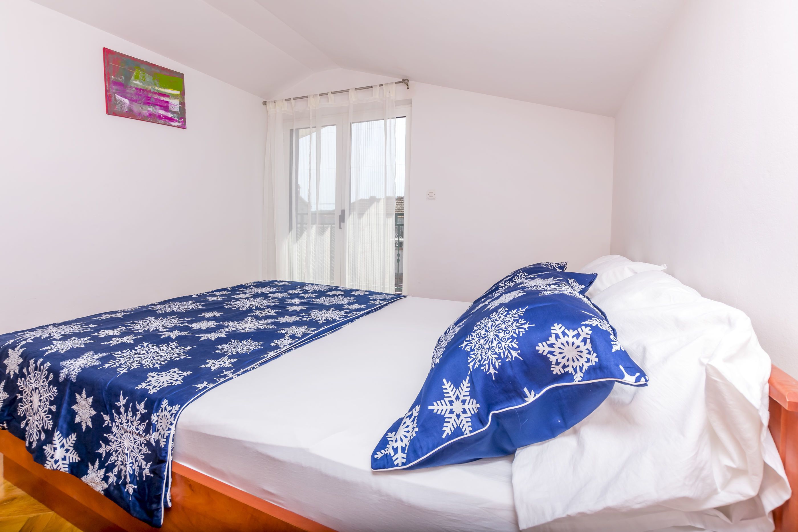 A single bed with a blue and white snowflake-patterned bedspread and pillow, a white mattress, and a wooden headboard.