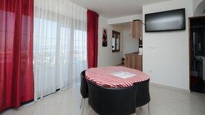 A room with a dining table, chairs, a TV, and a kitchen area.