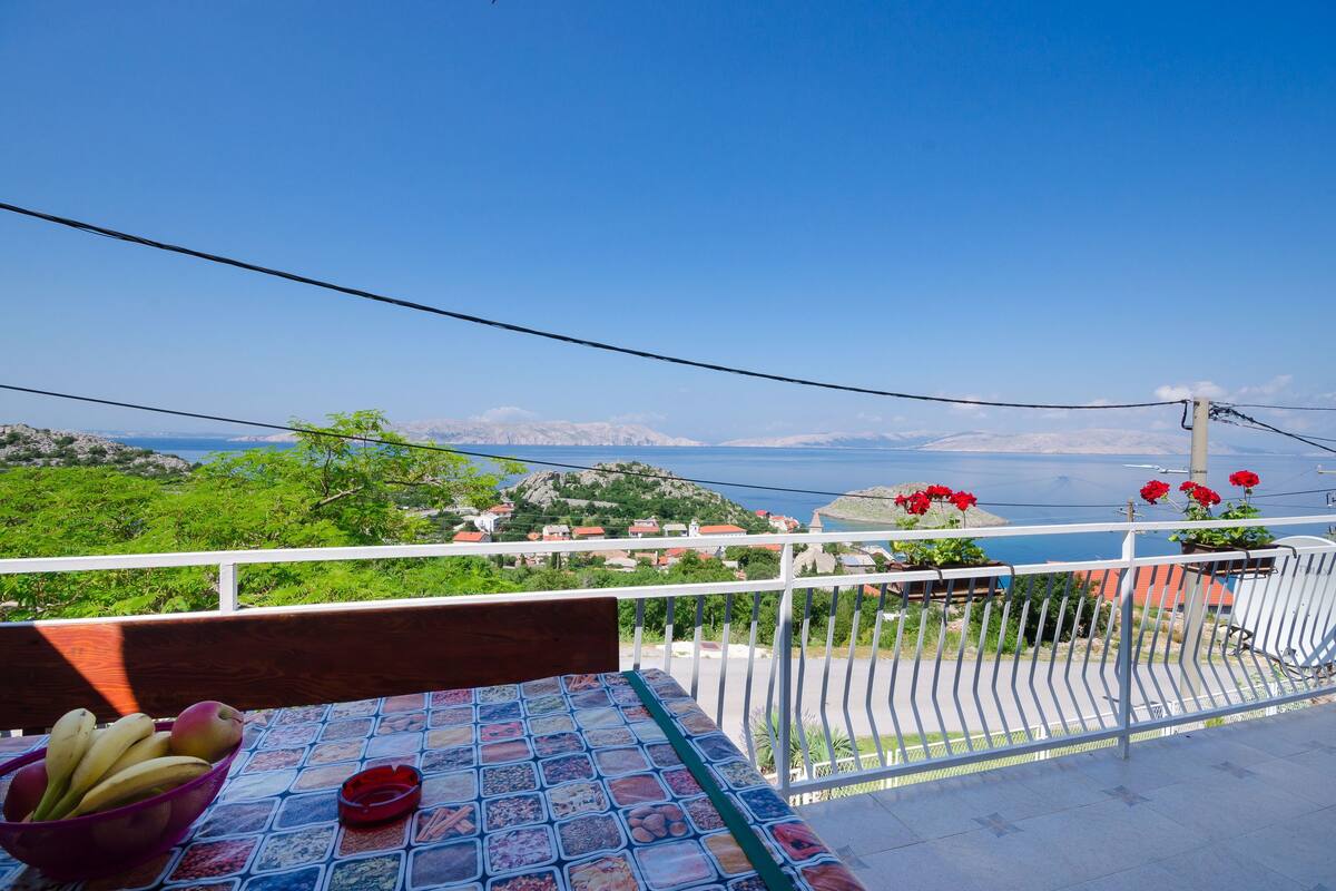 A balcony with a table, a bowl of fruit, and potted plants.