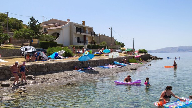A beach scene with clear water, people swimming, and colorful umbrellas.