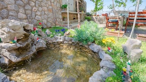 A stone building with a small pond, surrounded by potted plants and colorful flowers.