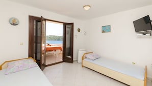 Une chambre avec deux lits, une télévision et une vue sur la mer, visible par une porte ouverte.
