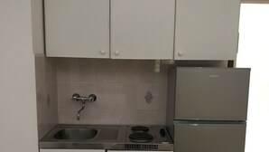 Une cuisine compacte avec des meubles blancs, un évier en acier inoxydable, une cuisinière encastrée et un réfrigérateur.
