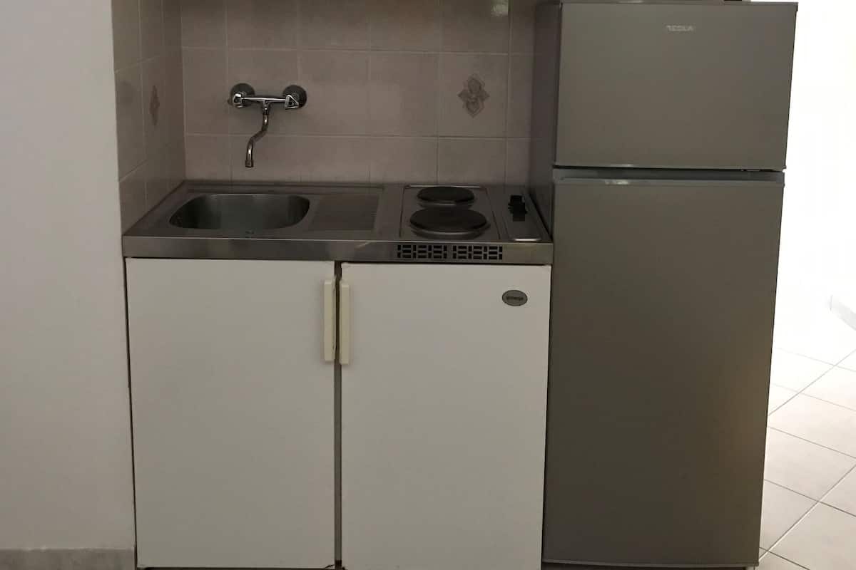 Μια μικρή, λειτουργική κουζίνα με λευκά ντουλάπια, έναν ανοξείδωτο νεροχύτη, μια εντοιχισμένη κουζίνα και ένα ψυγείο.