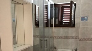 Une salle de bain avec une douche à parois de verre, un lavabo blanc, des toilettes et un miroir au-dessus du lavabo.